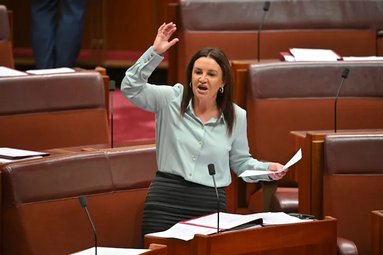 Senator Jacqui Lambie raising her right arm while speaking in Parliament.