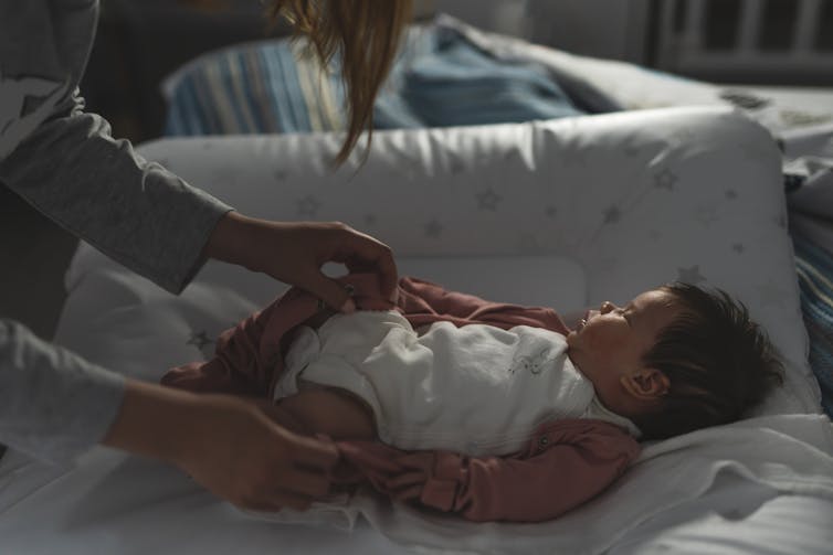 Mother caring for baby at night, baby asleep on changing mat