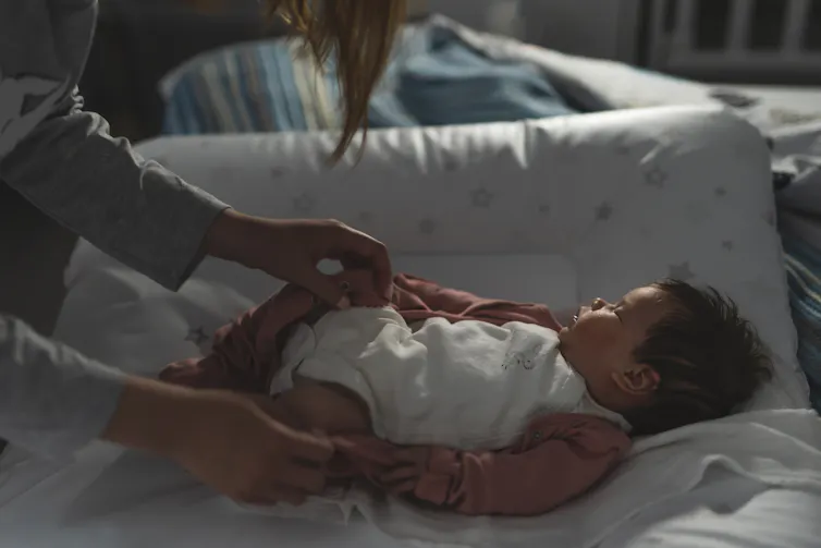 Mother caring for baby at night, baby asleep on changing mat