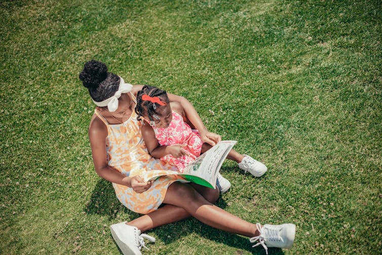 Two Black girls reading on the grass.