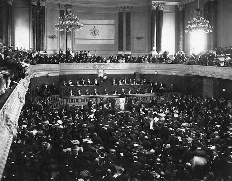 A black-and-white photo of a crowded hall and second-floor balcony encircling it.