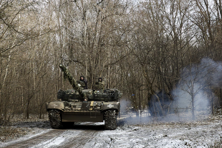 Soldiers driving a tank through a forest.