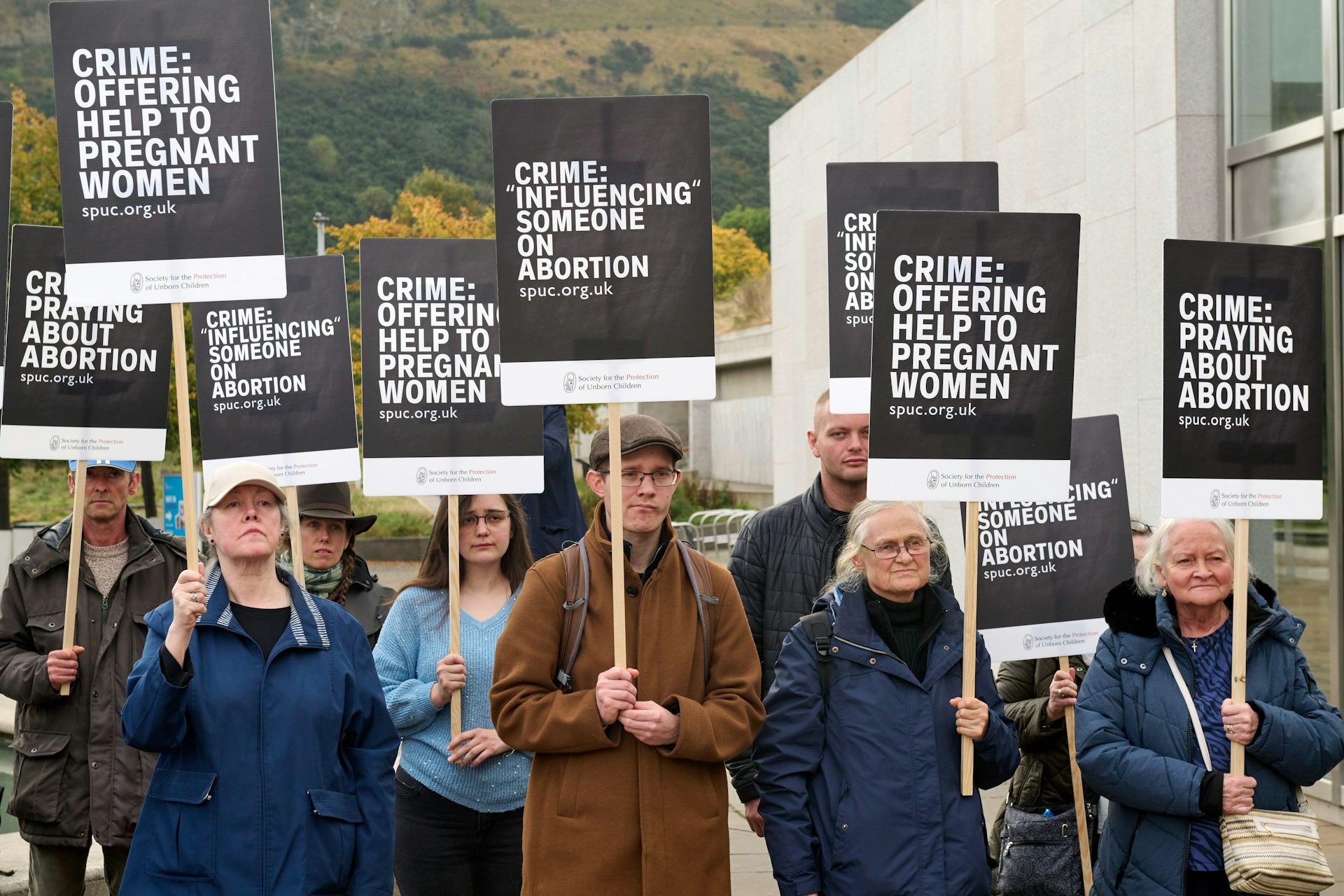 A group of people holding printed signs that list the various so-called crimes they believe fall under the safe access zones law.