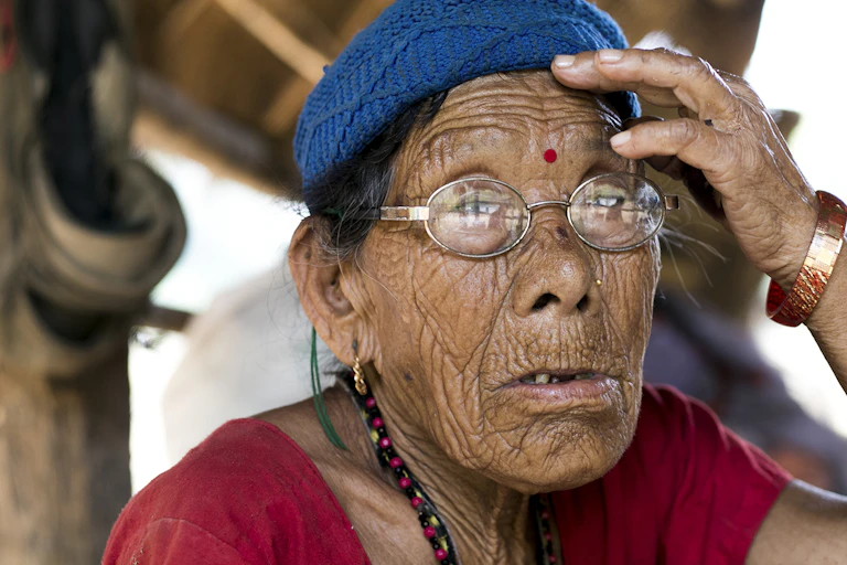 An elderly Nepalese woman wearing glasses, a blue knitted hat and bindi.