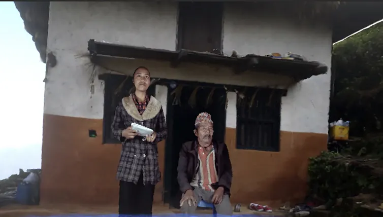 A young Nepalese girl standing with her grandfather, seated.