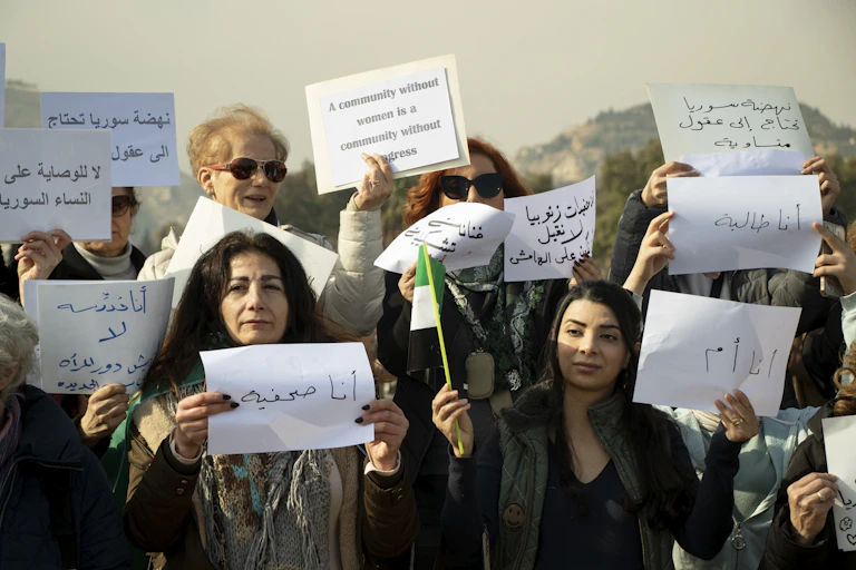 Syrian women protesters hold up banners in SYrian and English calling for greater rights.