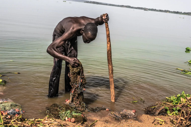 Um homem limpa sua rede de pesca às margens de um lago