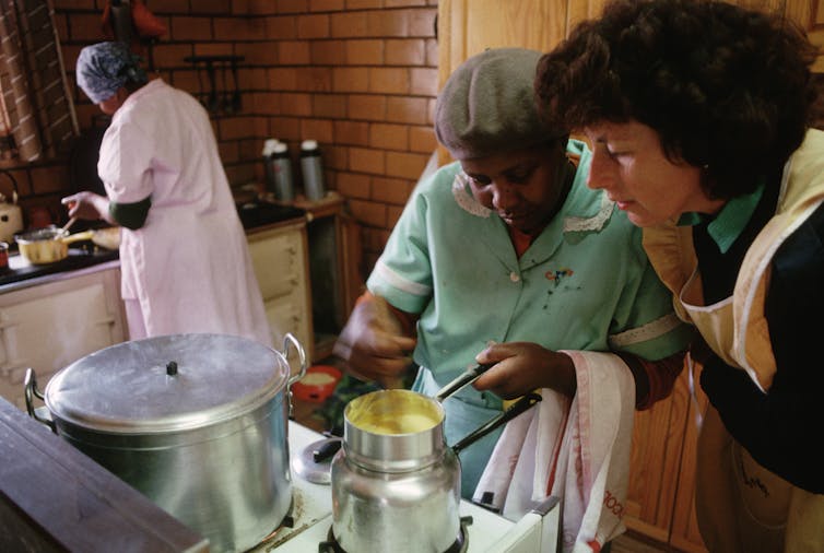 An employer supervises a domestic worker in the kitchen
