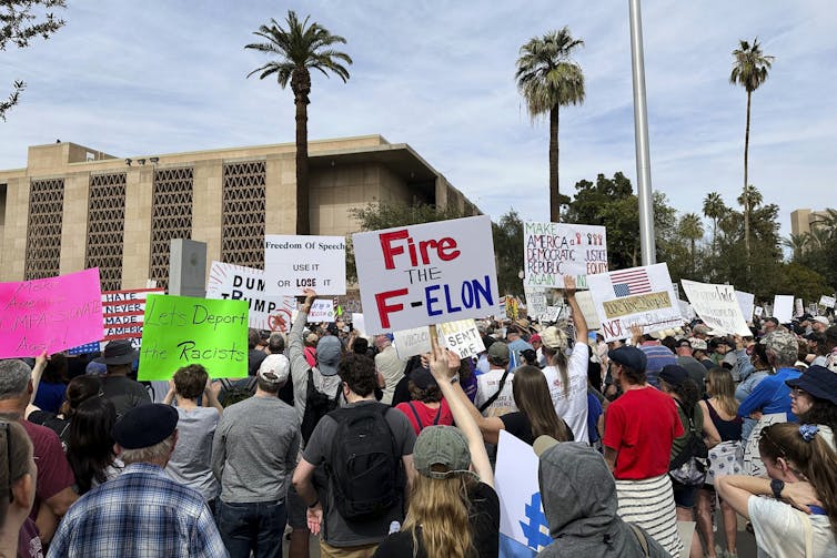 A group of people stand outside holding signs.