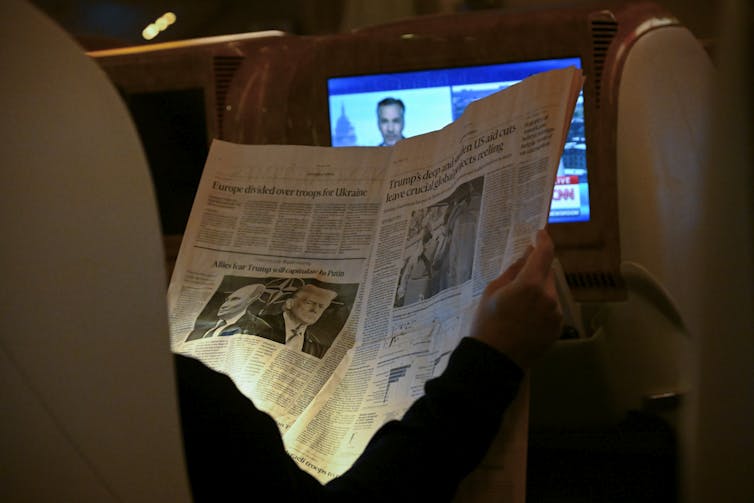 A person holds a newspaper that shows back-to-back profiles of two men in black and white.