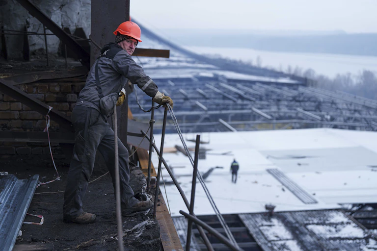 A man in an orange hard had stands looking down on a power plant.