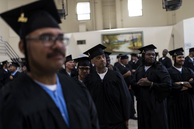 People in graduation caps and gowns stand together in a room.