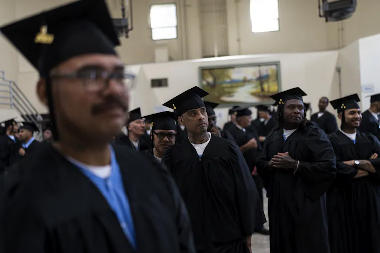 People in graduation caps and gowns stand together in a room.