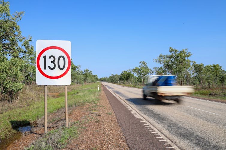 A motion blur of a ute driving along a road, passed a 130 kilometre per hour speed sign.