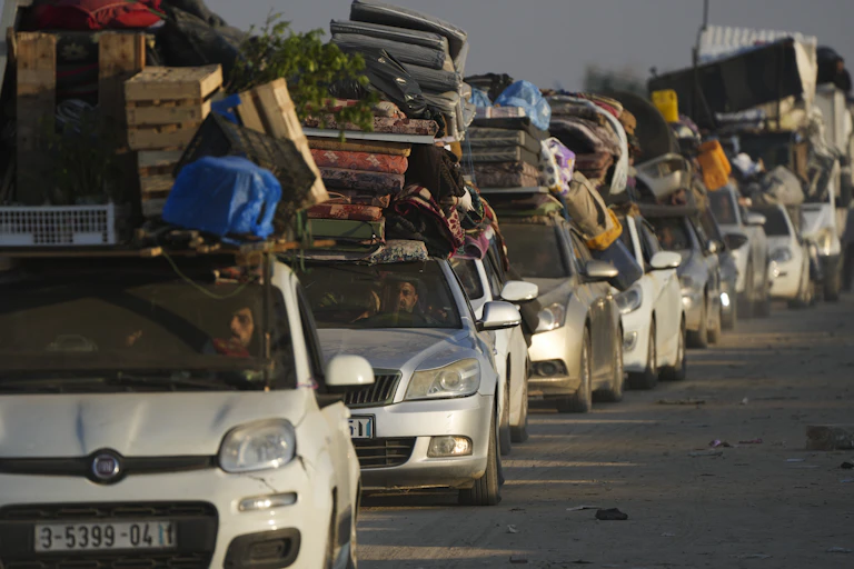 A row of cars with piles of furniture and suitcases piled on their roofs.