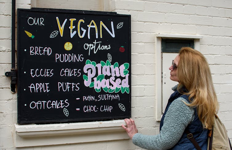 A woman looking at a vegan and vegetarian food menu blackboard outside a caf bar restaurant