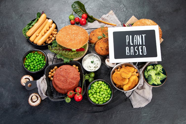 Plant-based foods including burgers, sausages and nuggets along with fresh vegetables and sauces, with a chalboard reading 'plant-based'