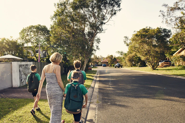 A woman walks three school children home along a suburban street.