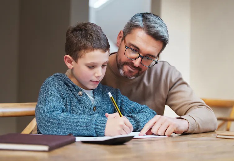 A man sits with a child writing in a notebook.