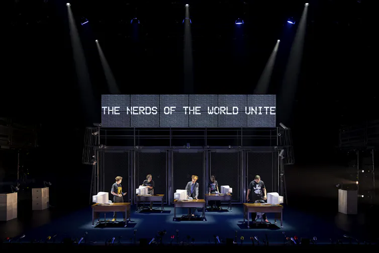 Actors at desktop computers. Text reads Nerds of the world unite.