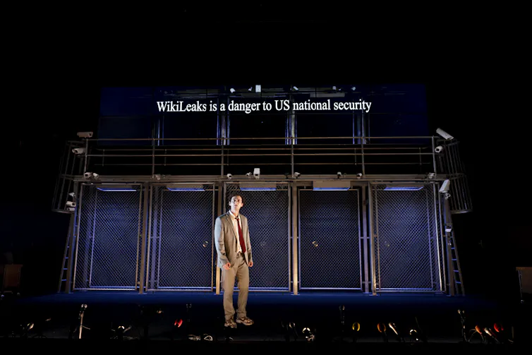 A man stands on stage. Text above reads WikiLeaks is a danger to US security.
