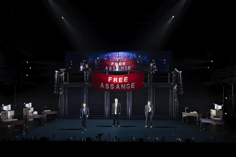 Wide shot of the stage. A banner reads Free Assange.