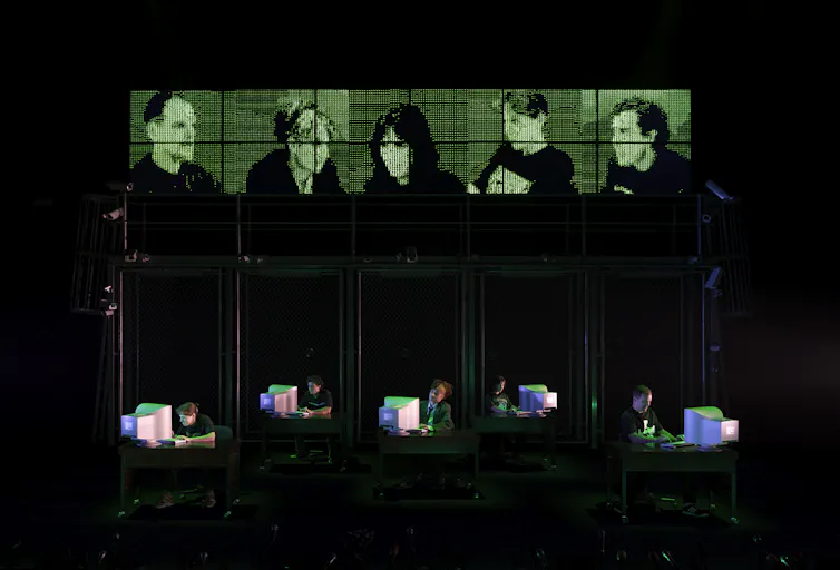 Actors sit at computers, above them their faces are replicated in green pixels.