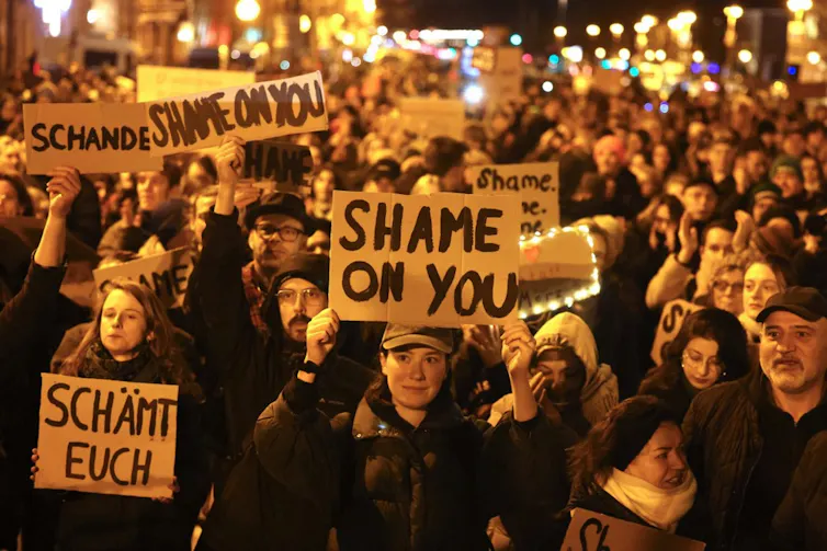 In the evening, a crowd of protesters with signs in German and English that read 'shame on you'