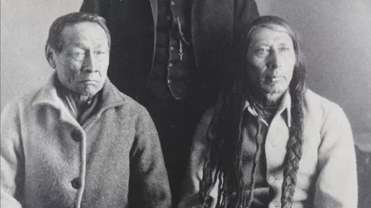 Two men seated, one with short hair and one with long hair.