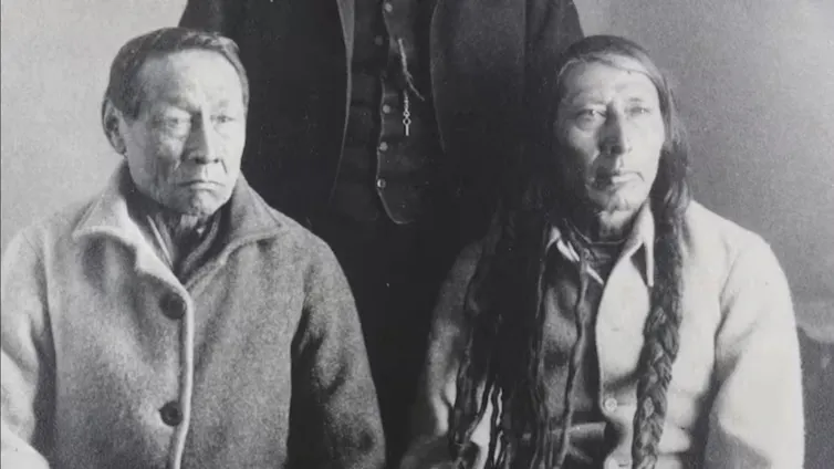 Two men seated, one with short hair and one with long hair.