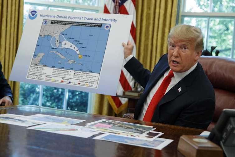 A man with orange-tinged hair holds up the map of a hurricane's path.