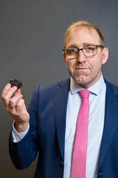 Man in suit holding small black mineral rock