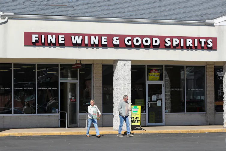 Man and woman crossing street in front of a store with sign that reads: Fine Wine & Good Spirits