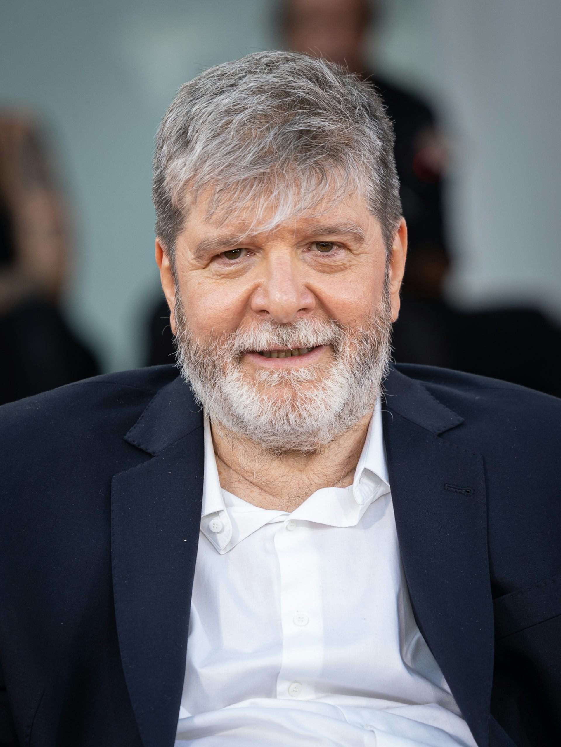 A middle-aged man with greying hair wearing a blue suit jacket and white shirt.