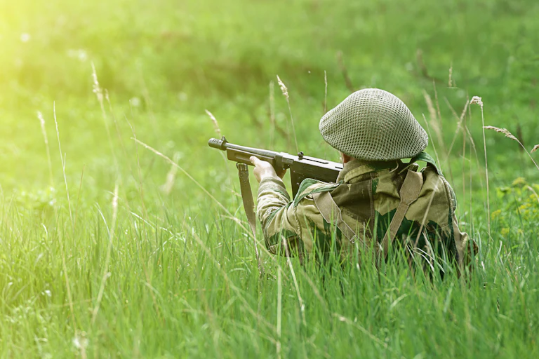 british soldier in long grass aiming an automatic weapon