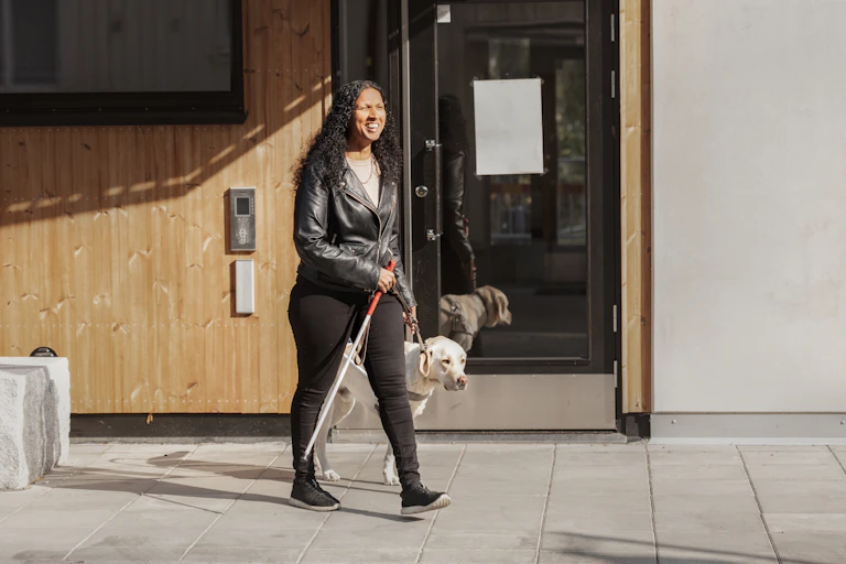 Visually impaired woman walking with guide dog and holding a white cane