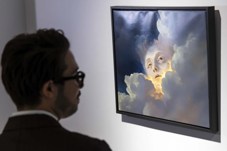 Photo of a man looking at a painting of a glowing face emerging from clouds.