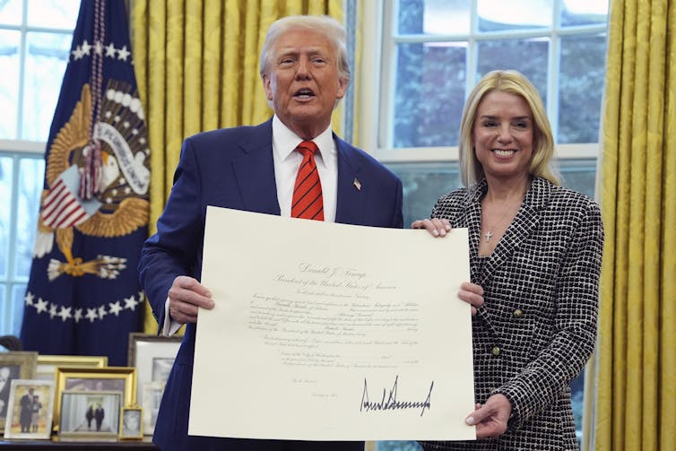 Man in suit stands holding large document with women in coat.