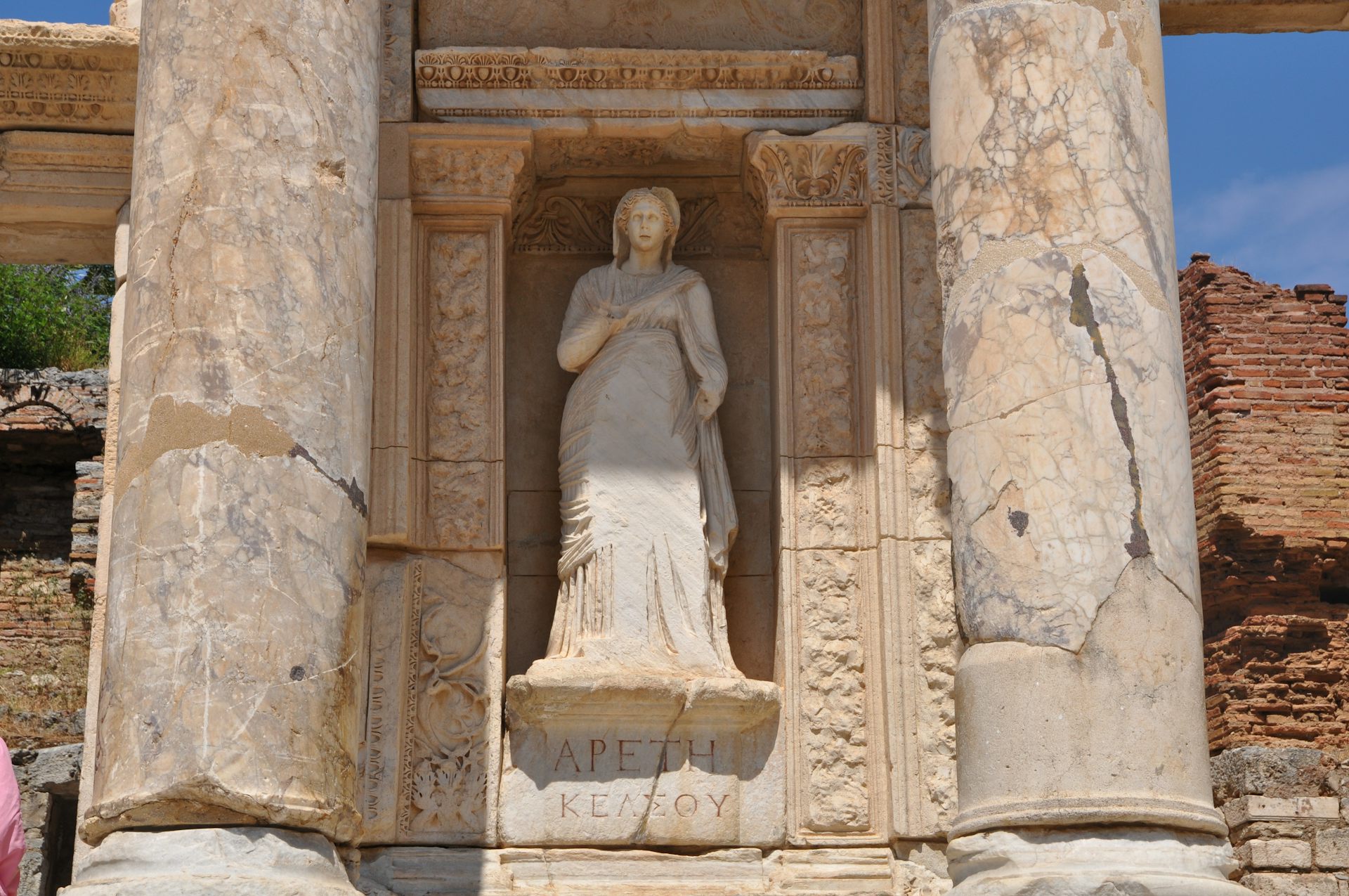 A statue of a woman in a long dress, set inside a niche in a wall with stone pillars in front of it.