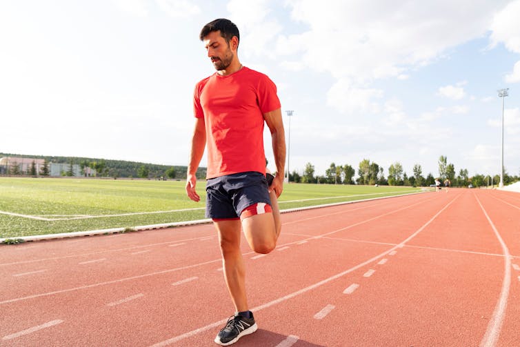 A man stretching his leg on a running track.