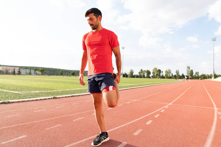 A man stretching his leg on a running track.