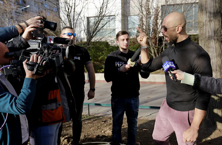 Andrew Tate shouting into a reporter's video camera.