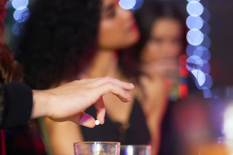 Photo en gros plan d'un homme droguant une femme qui boit en mettant un comprimé dans son verre, dans une boîte de nuit