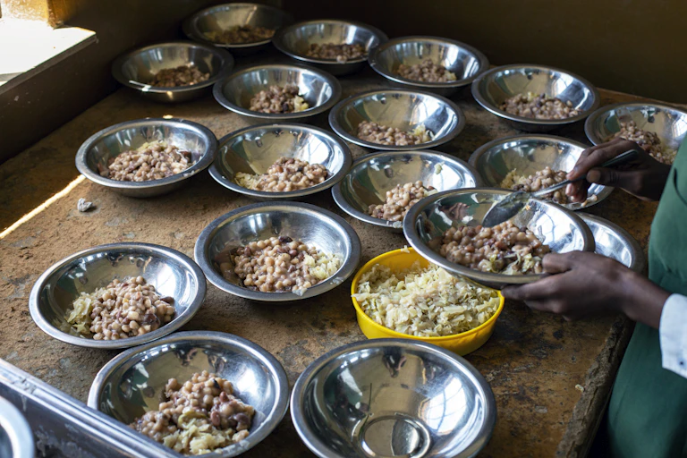 Metal dishes containing beans, on a table, with someone serving a spoonful into a dish