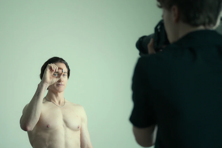Fit, shirtless man holds up a pill in front of his face.