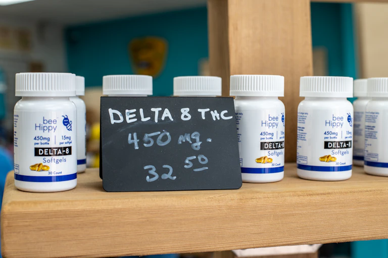 Half a dozen white plastic bottles are lined up on a counter behind a sign that reads "DELTA 8 THC: 450 mg, $32.50."