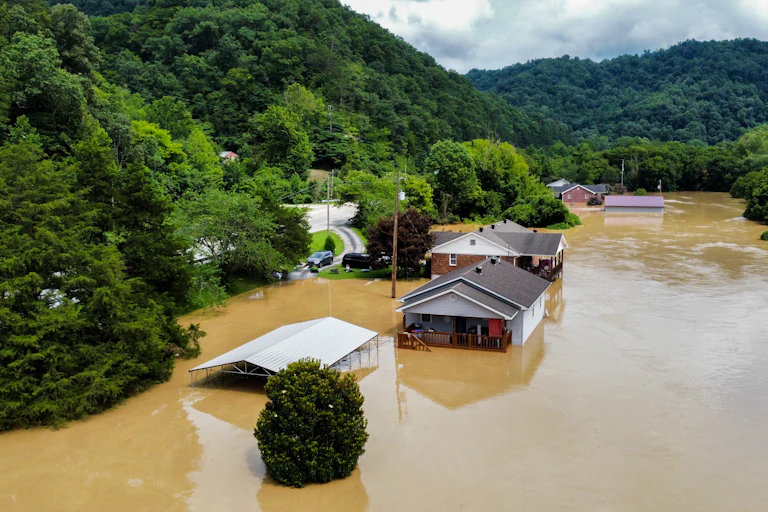 Flooded homes along a river in an narrow area between mountains.