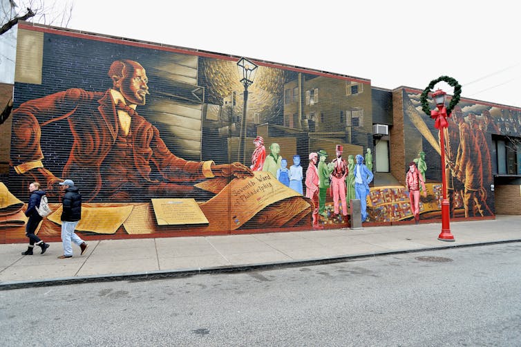 Colorful mural depicting Black man in three-piece suit circa 1900 at desk with papers and books, and people standing in street to his right