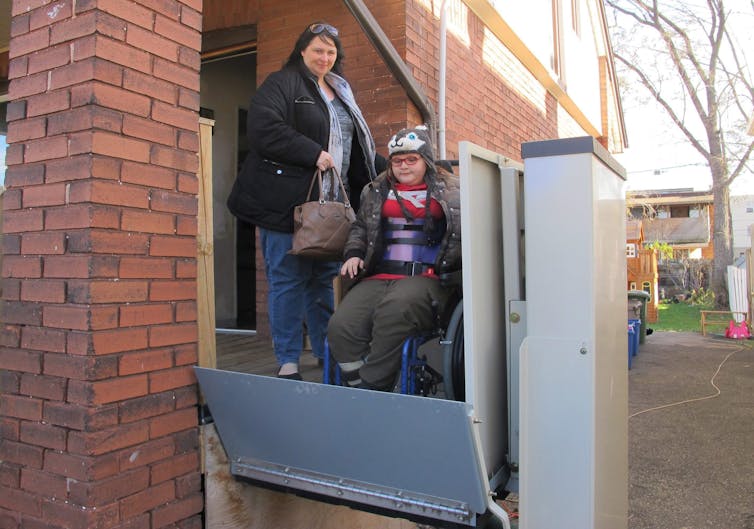 In a wheelchair, a woman and a teenage girl uses a lift for wheelchairs in wheelchairs.