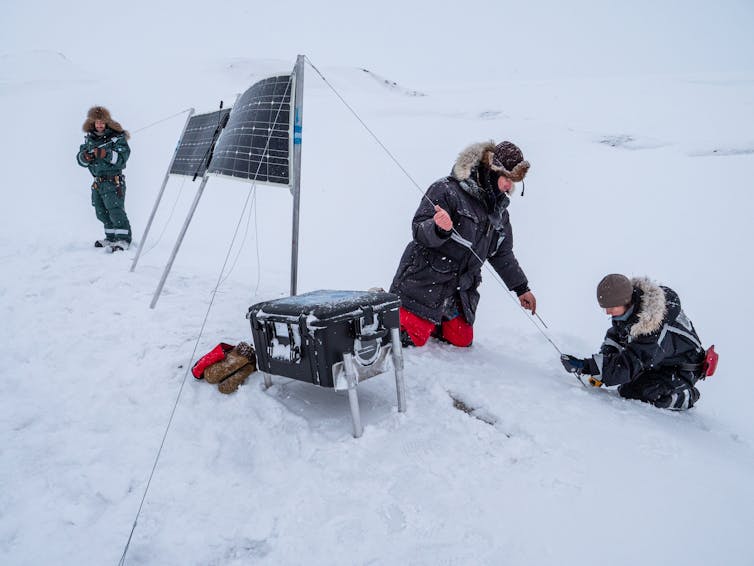 three people setting up a time-lapse camera in the snow